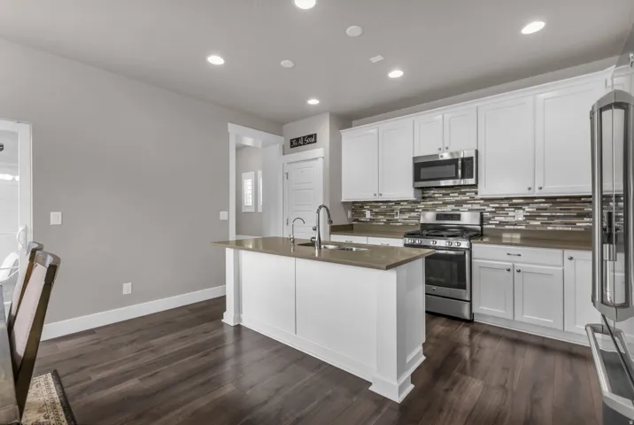 Kitchen featuring white shaker cabinetry, stainless steel appliances, a multi-tone tile backsplash, and an island with an undermount sink