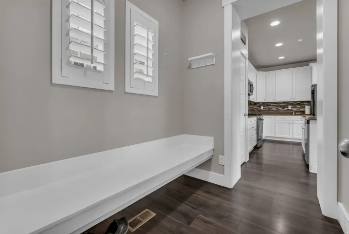 Built-in bench with storage, wood-finish flooring, white plantation shutters, white kitchen cabinetry, and recessed lighting