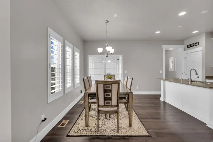 Dark wood-finish flooring, recessed lighting, white window shutters, white cabinetry, and a kitchen island with a double sink