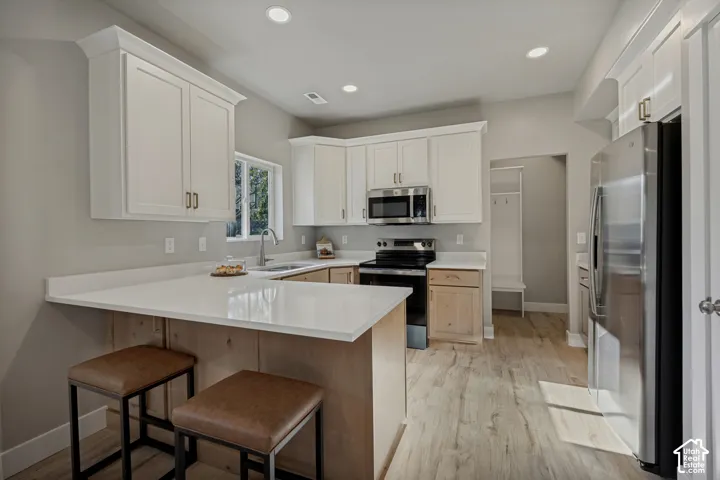Kitchen featuring white upper cabinetry, wood-finish lower cabinetry, a stainless steel microwave and stove, a stainless steel refrigerator, and wood-finish flooring