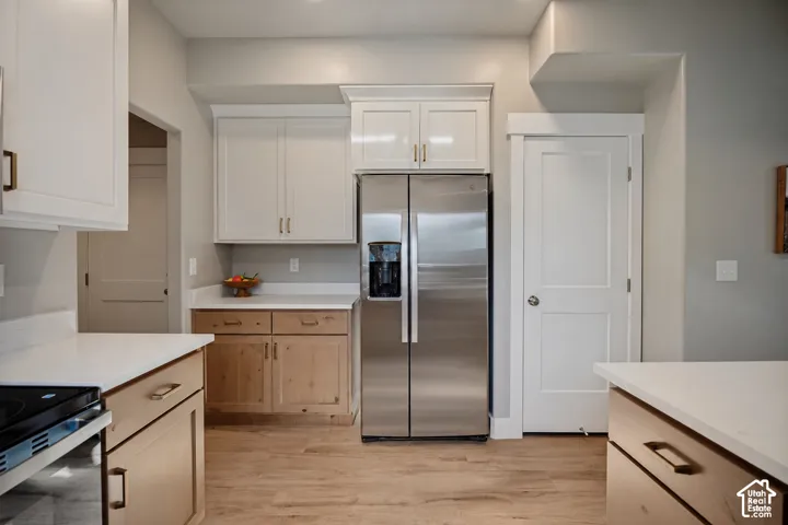Stainless steel side-by-side refrigerator, mixed-tone cabinetry with white upper and natural wood-tone lower cabinets, light-toned countertops, and wood-finish flooring