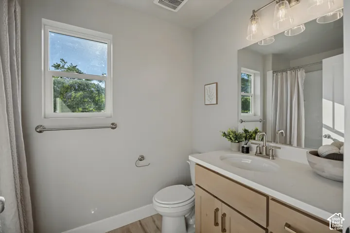 Contemporary bathroom featuring a single window, a vanity with light wood-finish cabinetry, a white countertop with an undermount sink, and a brushed nickel light fixture