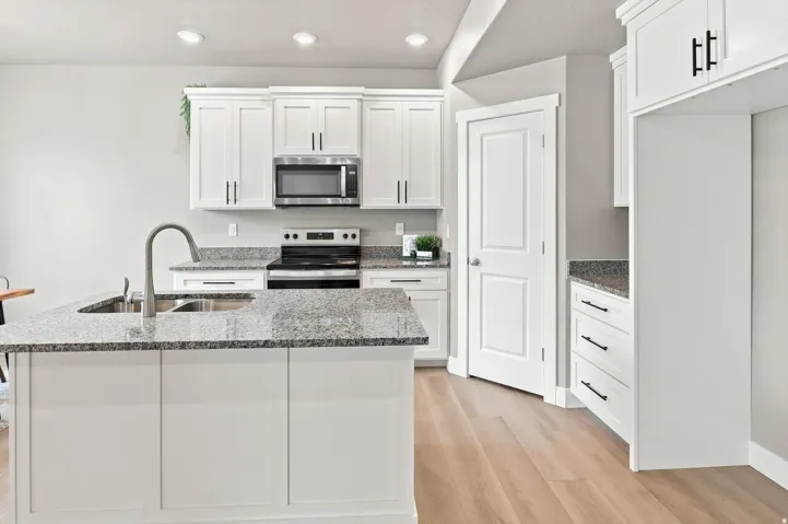 White shaker cabinetry, granite countertops, stainless steel appliances, wood-finish flooring, and recessed lighting