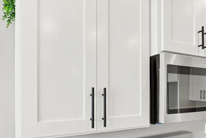White shaker-style cabinetry with matte black hardware and a stainless steel microwave