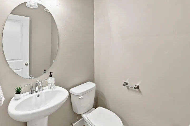 Pedestal sink with chrome faucet, oval mirror, and overhead vanity lighting