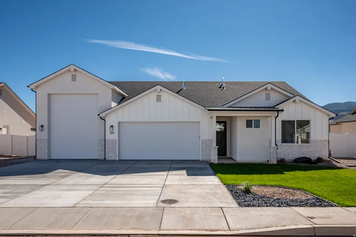 White exterior with board and batten accents, a two-car garage, an additional single-car garage, a dark asphalt shingle roof, and a concrete driveway