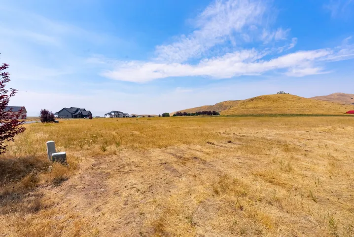 Expansive undeveloped land featuring a clear blue sky, distant residential structures, and rolling hills