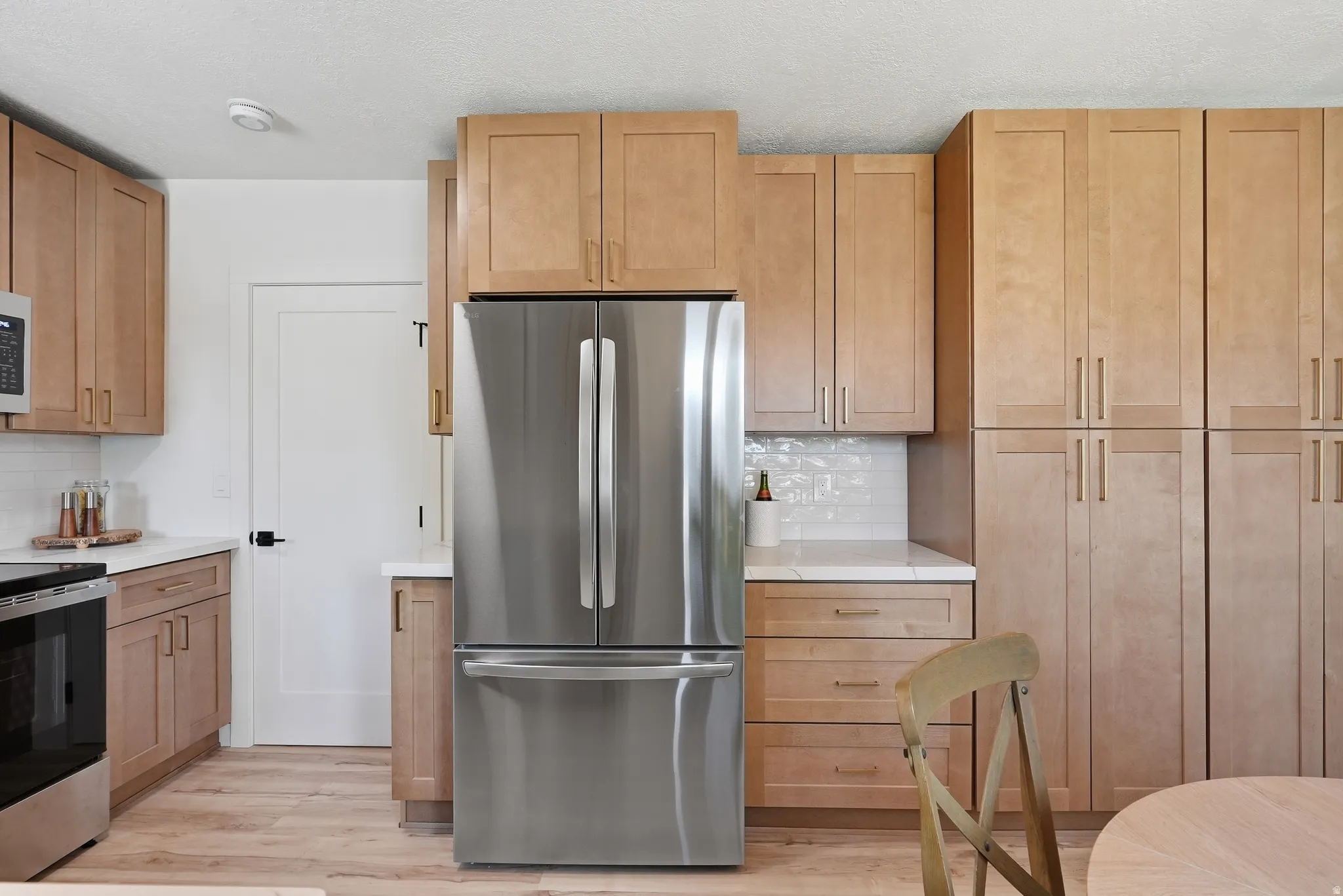 Kitchen featuring wood-finish cabinetry, stainless steel refrigerator, white countertops, white subway tile backsplash, and wood-finish flooring