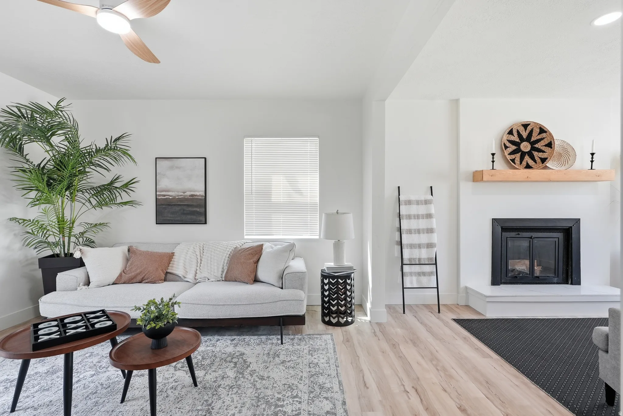Living area with wood-finish flooring, a white-painted fireplace with a wood mantle, and a built-in ceiling fan with integrated lighting