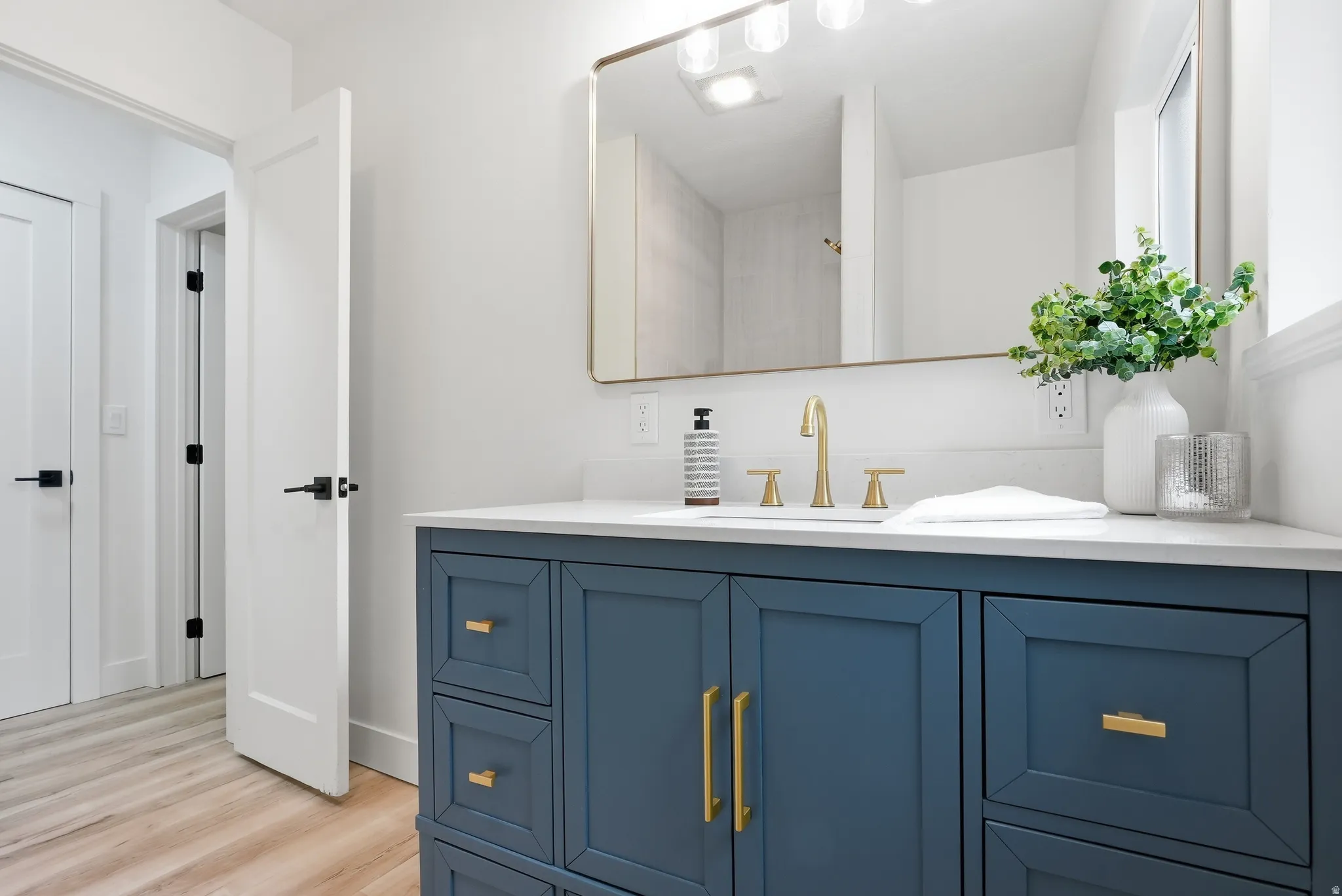 Blue vanity with gold hardware, white countertop, gold-finish faucet, and modern rectangular mirror with integrated lighting