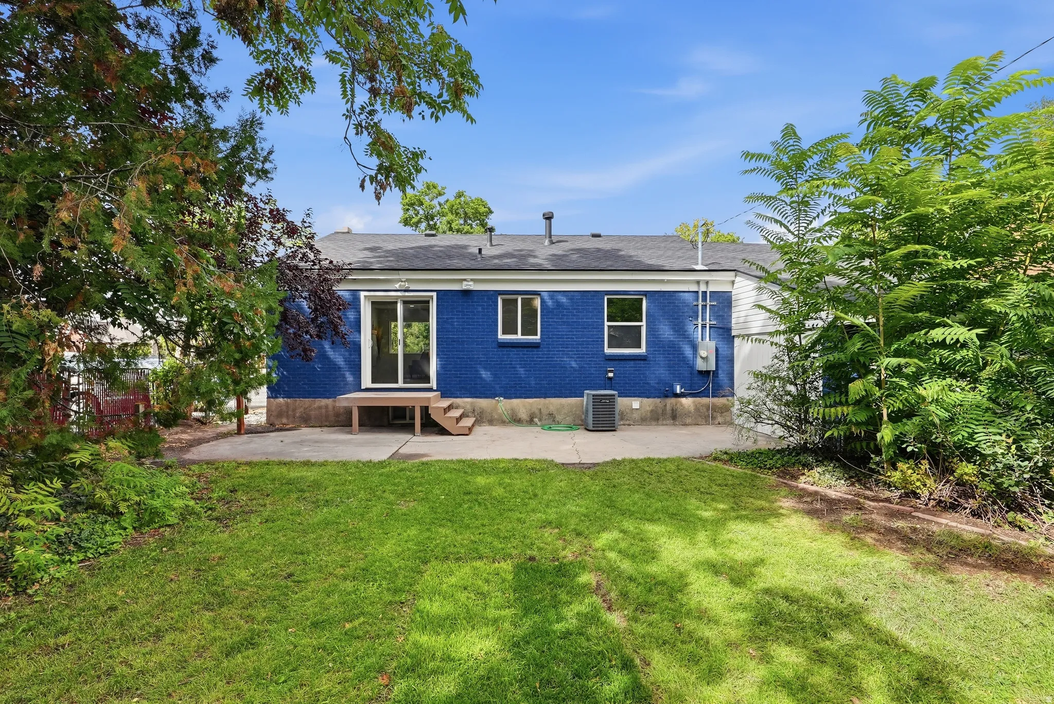 Expansive green lawn with mature perimeter trees, concrete patio, and rear exterior access via sliding glass doors