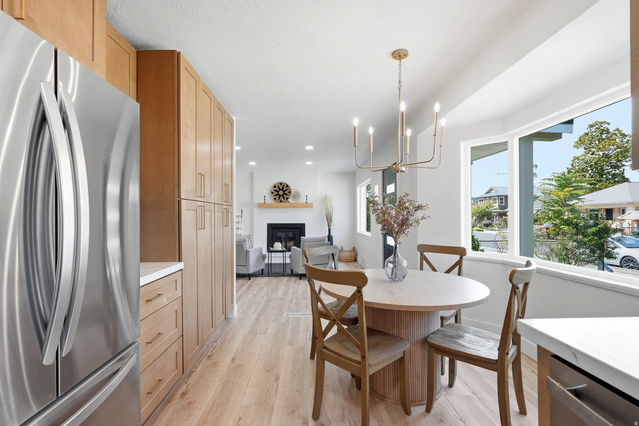 Stainless steel refrigerator, full-height light wood-finish cabinetry, light wood-finish flooring, bay window, and a bronze chandelier