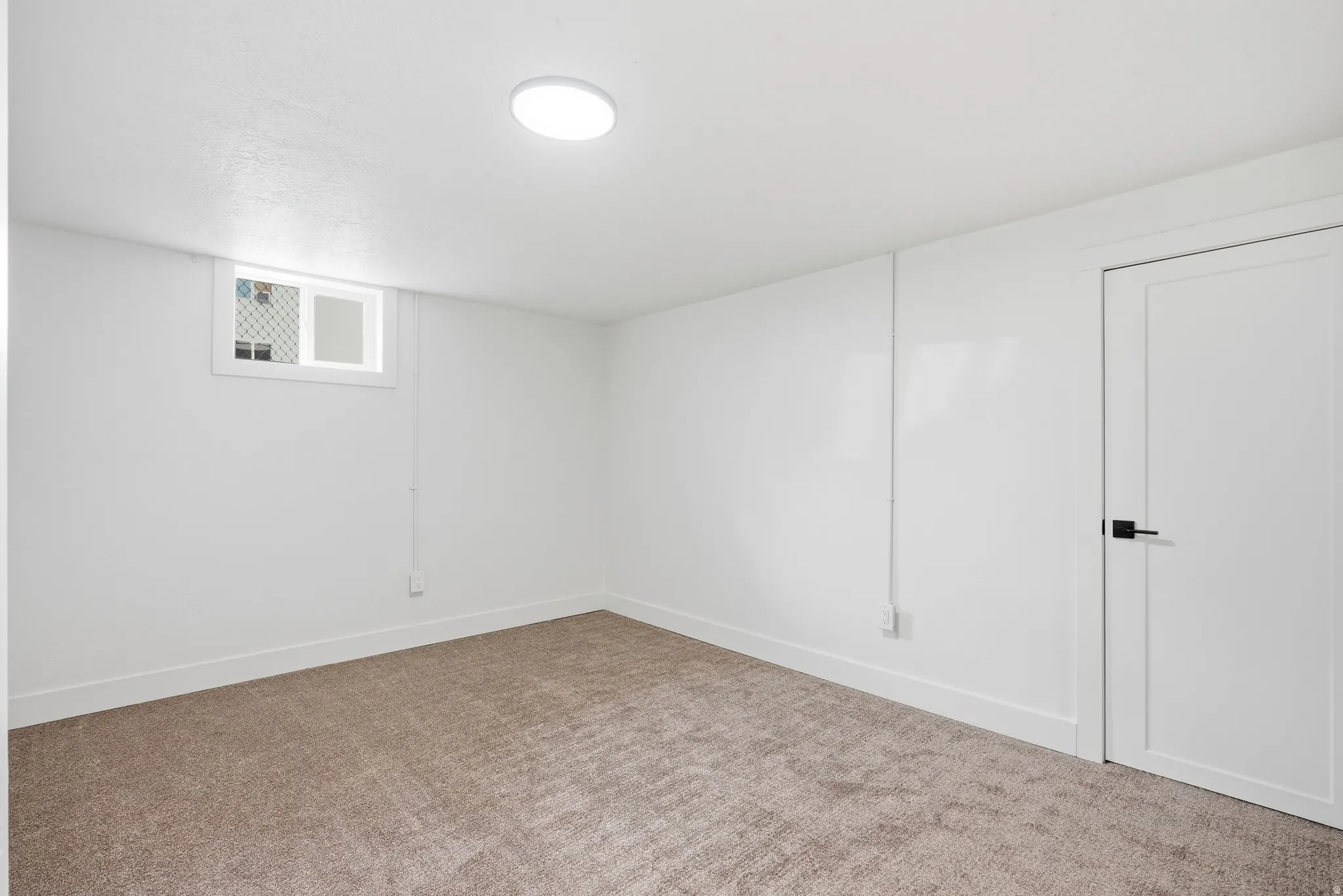 Neutral wall paint, plush carpet flooring, recessed ceiling light fixture, white trim, and a white interior door with black hardware