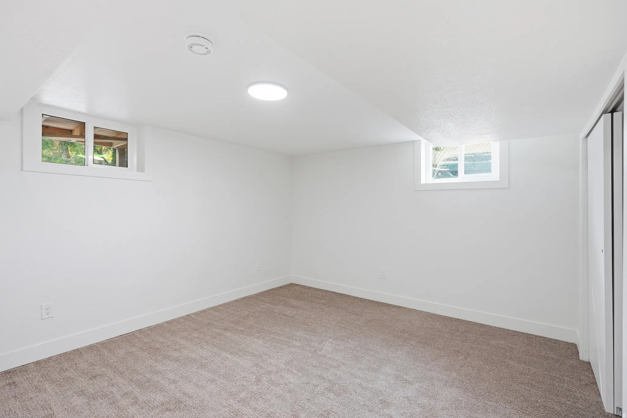 Recessed lighting and a circular ceiling light illuminate this carpeted room with multiple windows