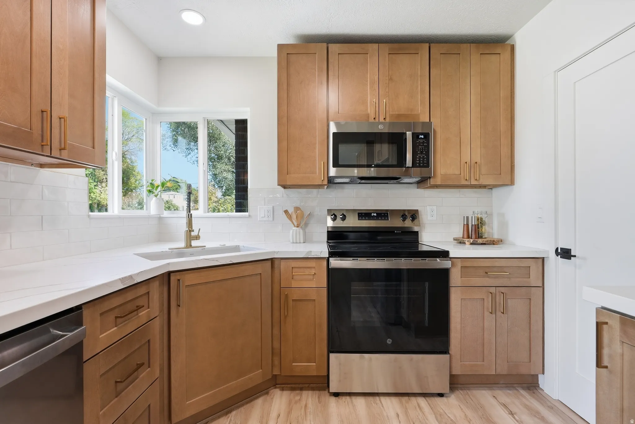 Kitchen featuring light wood-finish cabinetry, white countertops, subway tile backsplash, stainless steel appliances, and a corner window