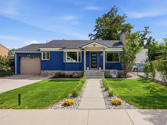 Blue exterior with white trim, a dark asphalt shingle roof, attached garage, and a concrete pathway leading to the front entry