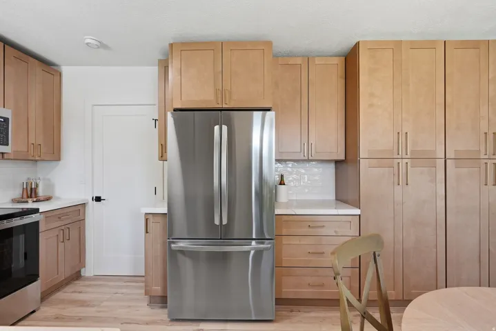 Kitchen featuring wood-finish cabinetry, stainless steel refrigerator, white countertops, white subway tile backsplash, and wood-finish flooring