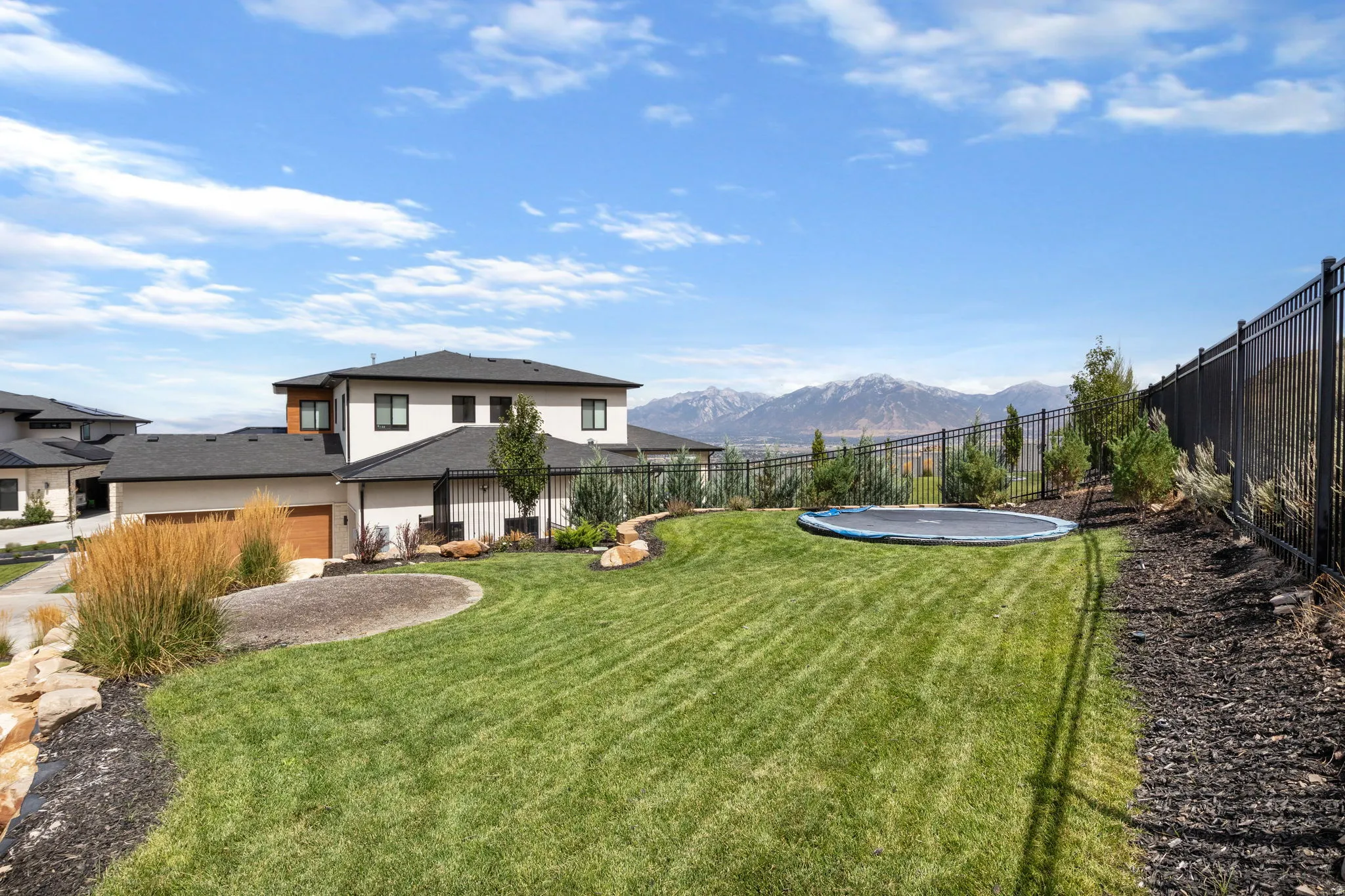 Expansive manicured lawn with a dark metal fence, mature landscaping, and mountain scenery