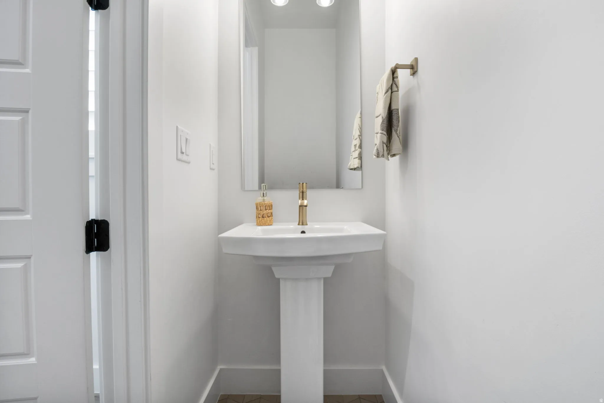 Pedestal sink with a gold-tone faucet, framed mirror, and recessed lighting