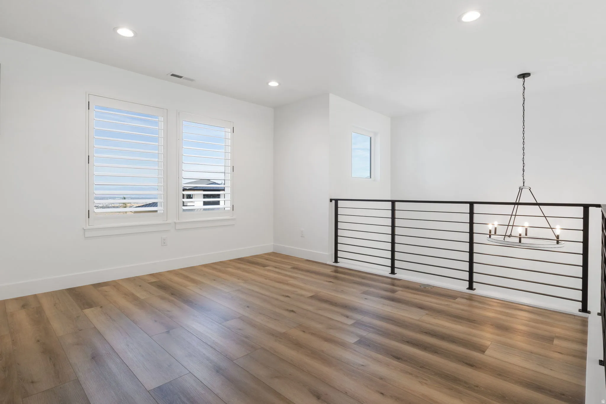 Open loft area with wood-finish flooring, recessed lighting, and a contemporary chandelier