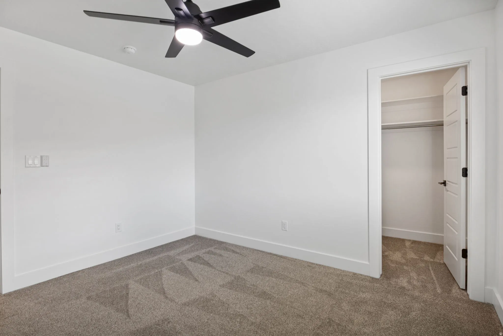 Neutral-toned carpet flooring with white walls and a contemporary black ceiling fan