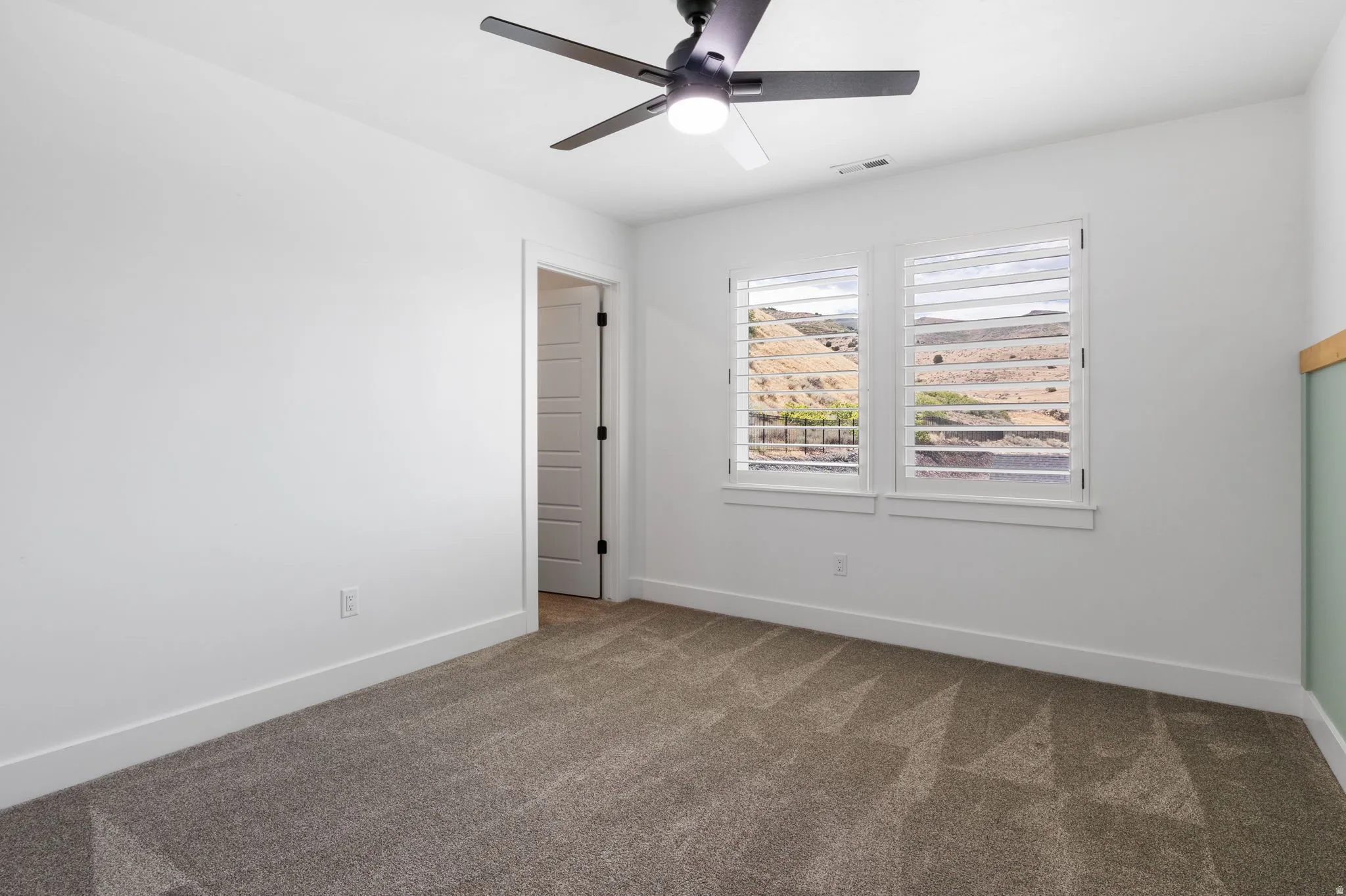 Recessed lighting, ceiling fan with integrated light, two windows with plantation shutters, mountain landscape, and carpeted flooring