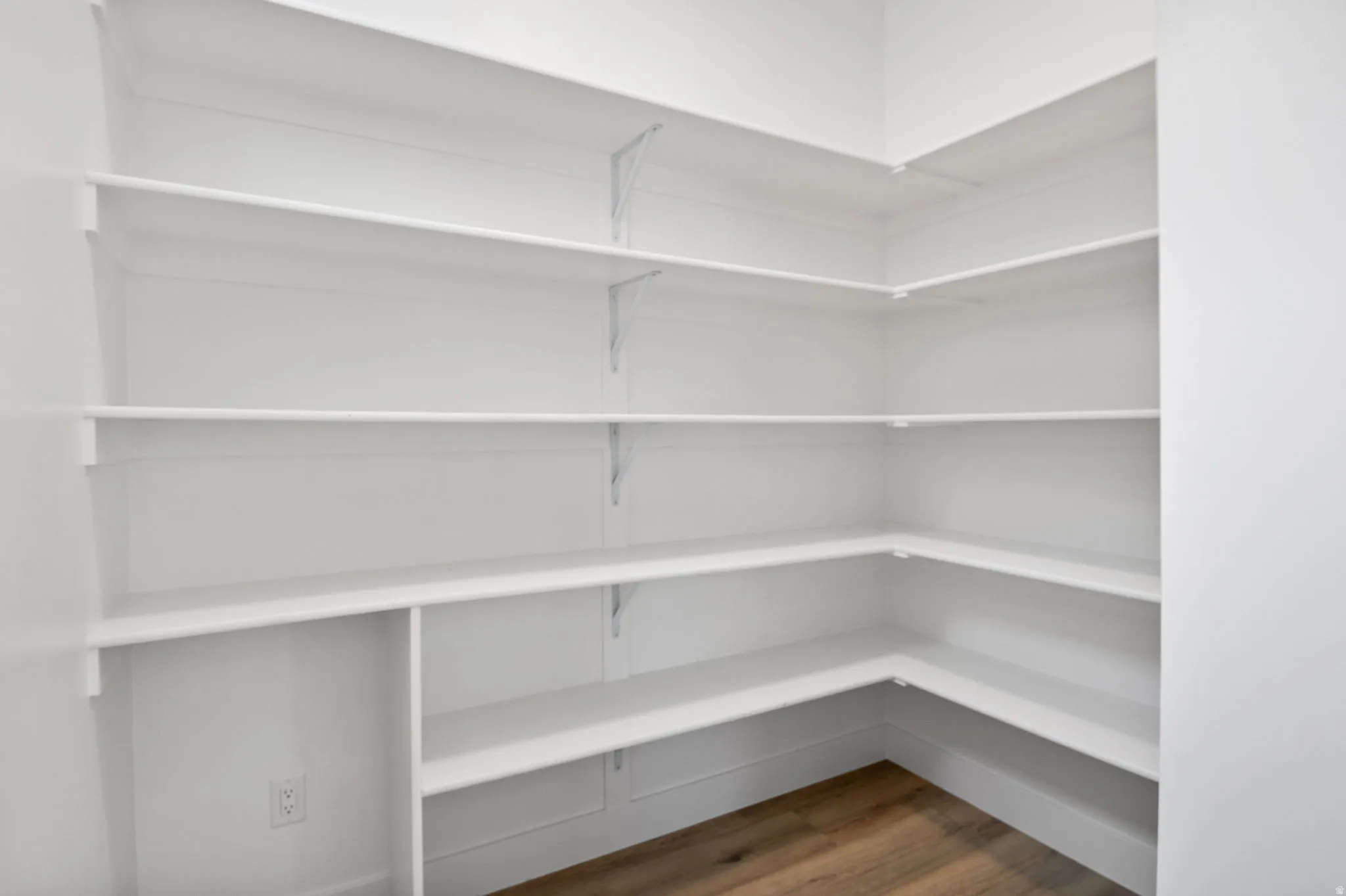 White built-in shelving, multi-level shelving, corner shelving, wood-finish flooring, and white walls