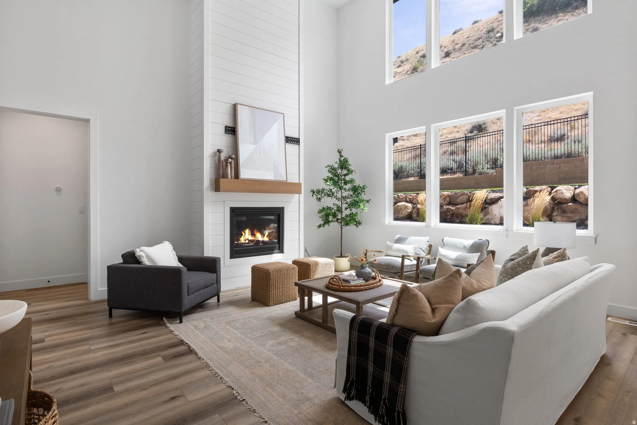 Vaulted ceilings, wood-finish flooring, a shiplap fireplace with a wood mantle, and multiple large windows