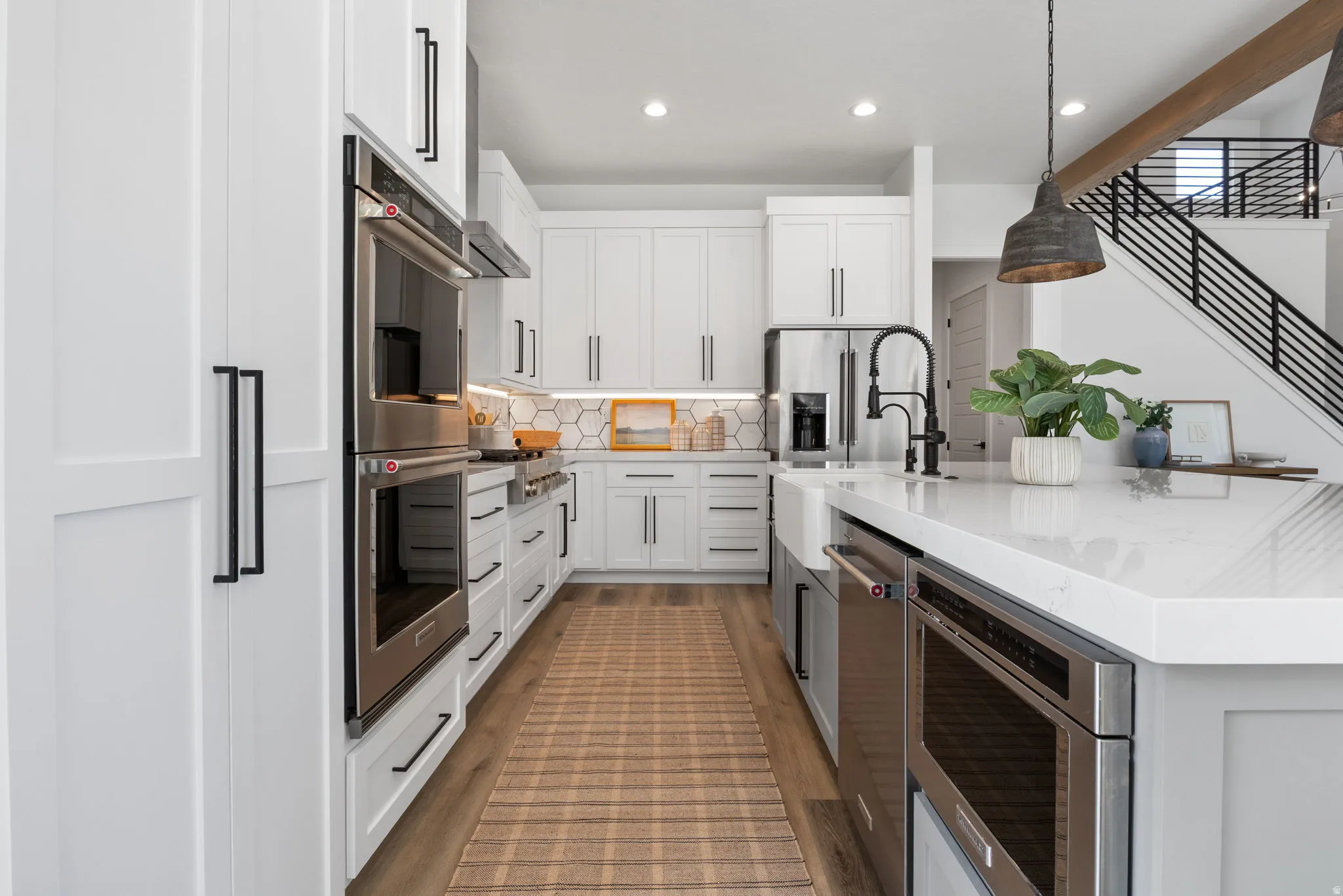 Gourmet kitchen with white cabinetry, stainless steel appliances, hexagon tile backsplash, and an expansive island with a farmhouse sink