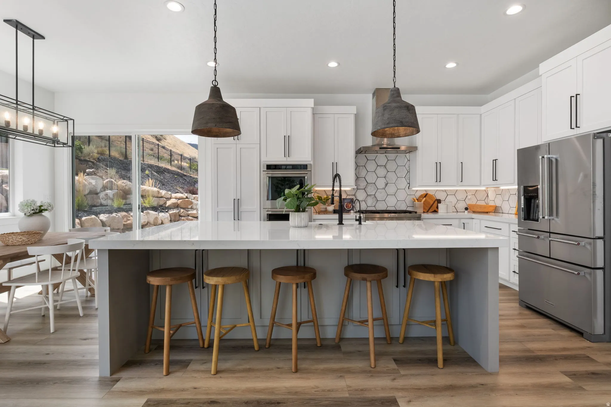 Modern kitchen featuring an expansive island with a light-toned countertop, stainless steel appliances, white cabinetry, and wood-finish flooring