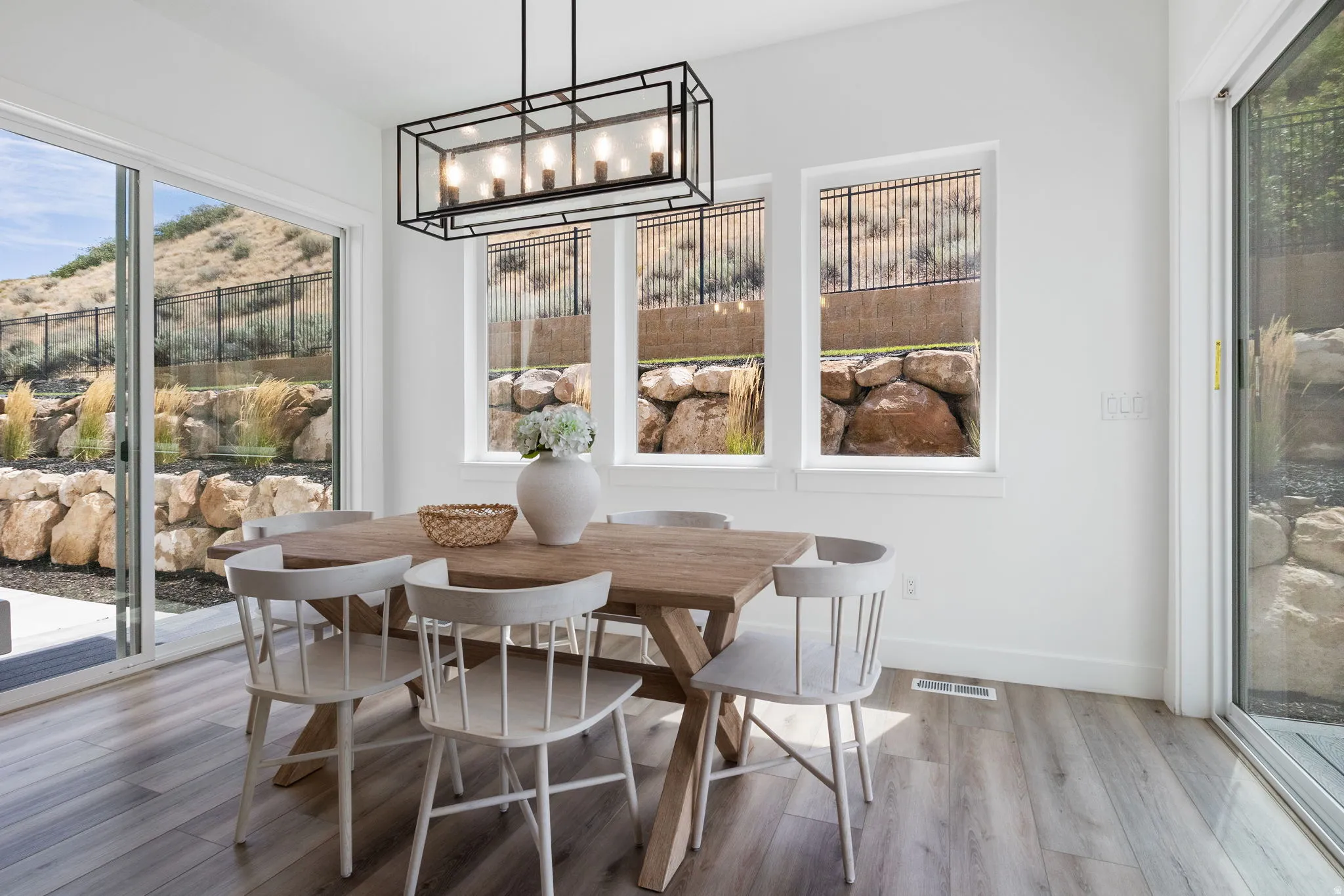 Wood-finish flooring, white walls, and a linear black chandelier illuminate the dining space