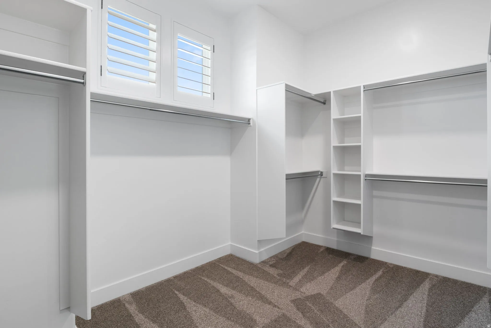 Built-in white shelving, integrated hanging rods, white shuttered windows, and patterned carpet flooring