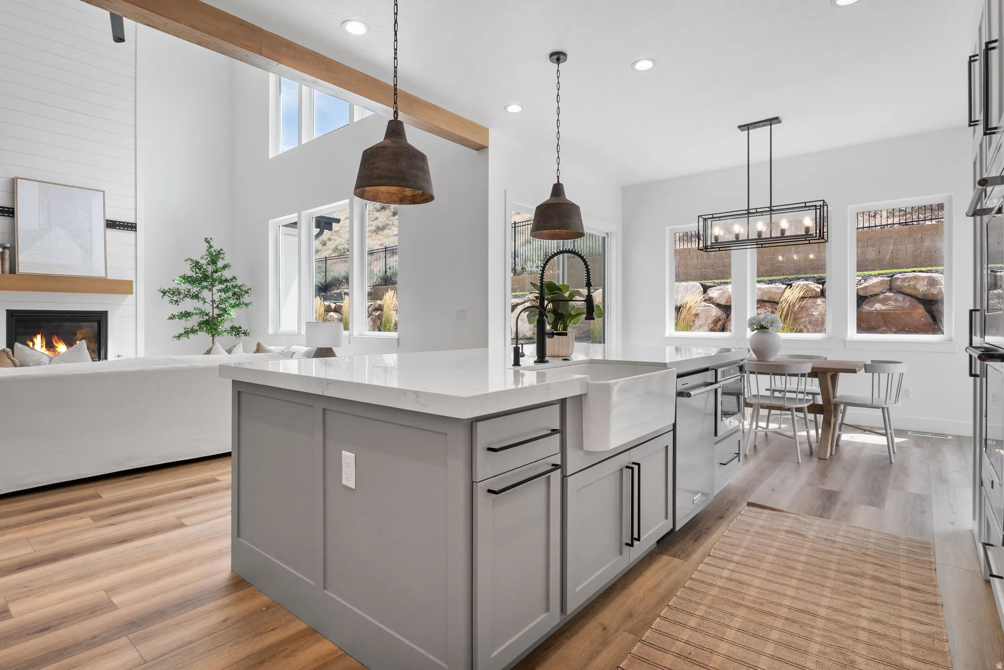 Vaulted ceiling with exposed beam, fireplace with shiplap surround, kitchen island with built-in farmhouse sink, stainless steel appliances, and recessed lighting