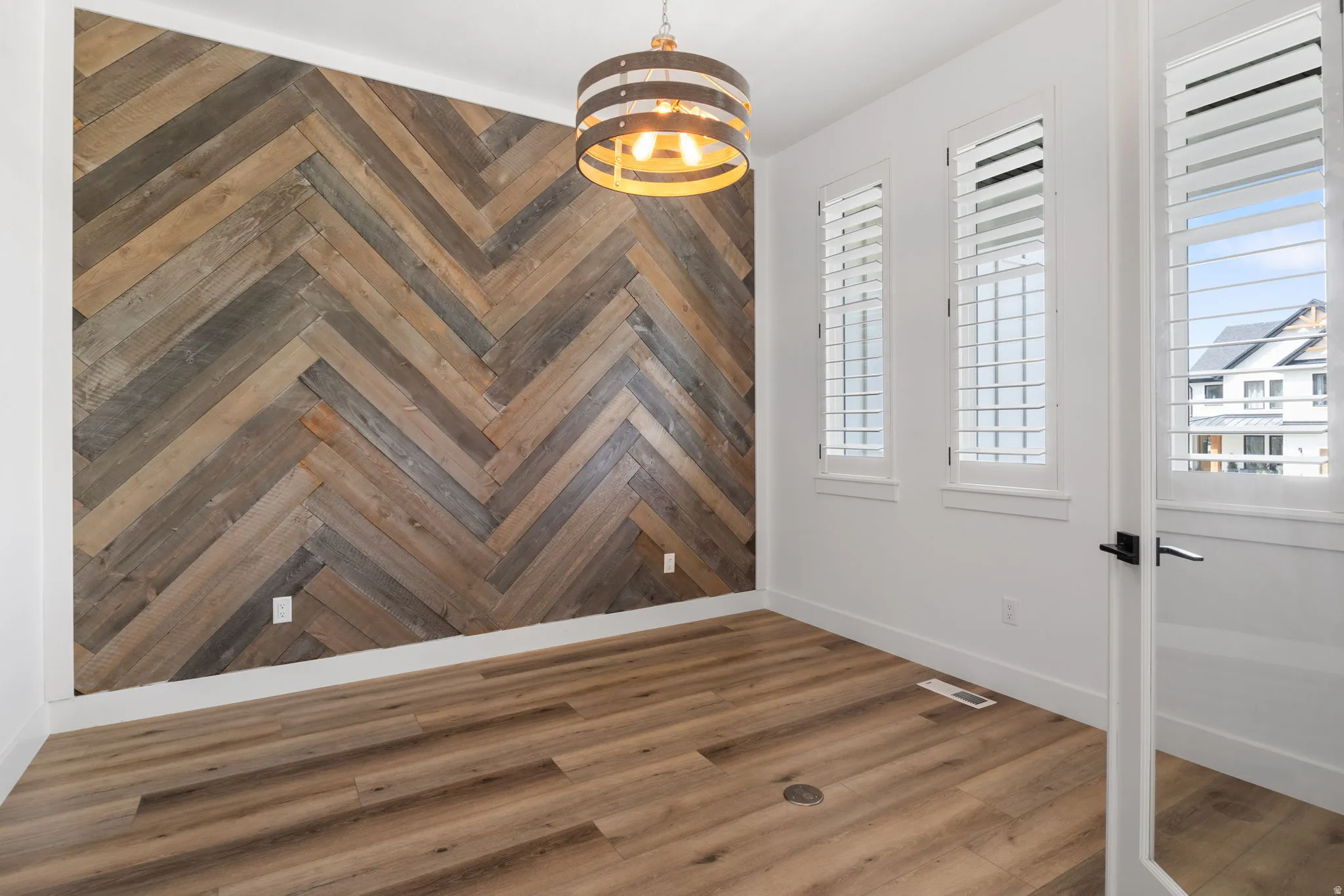 Herringbone wood-finish accent wall with wood-finish flooring, white walls, and three windows with white plantation shutters
