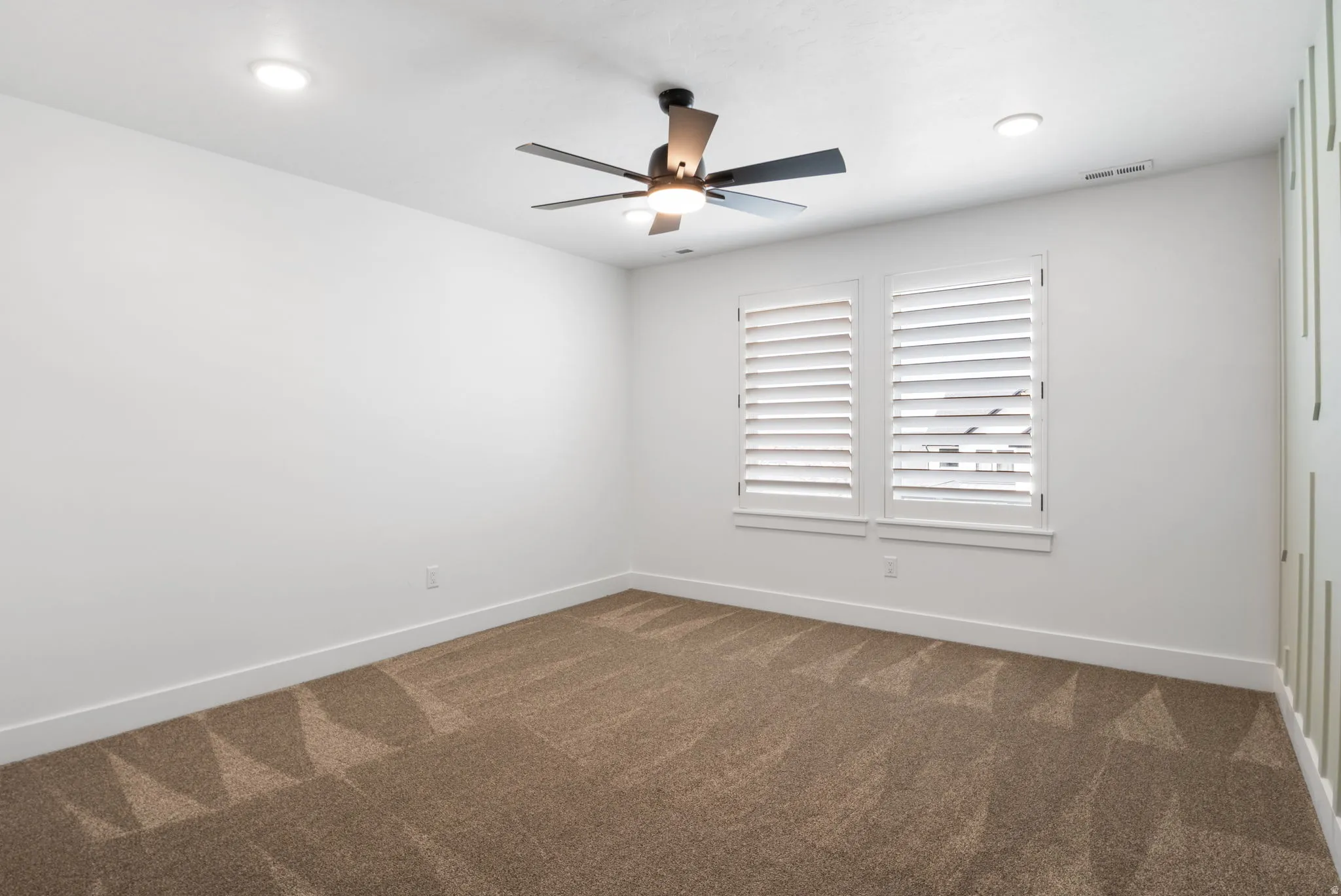 Recessed ceiling lighting, ceiling fan, window with plantation shutters, broad baseboards, and patterned carpeting
