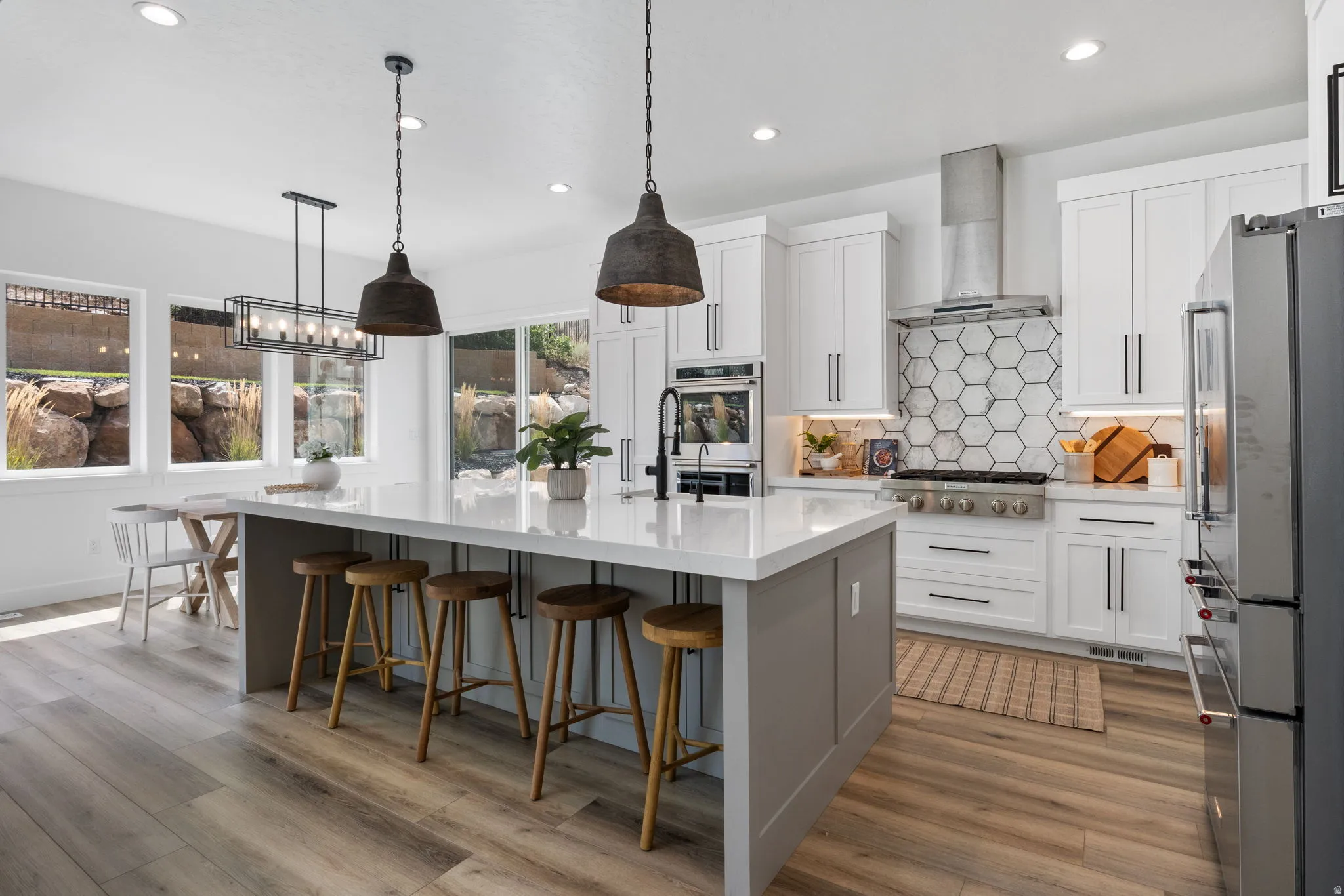 Gourmet kitchen with wood-finish flooring, white cabinetry, a large kitchen island with counter seating, stainless steel appliances, and a hexagonal tile backsplash