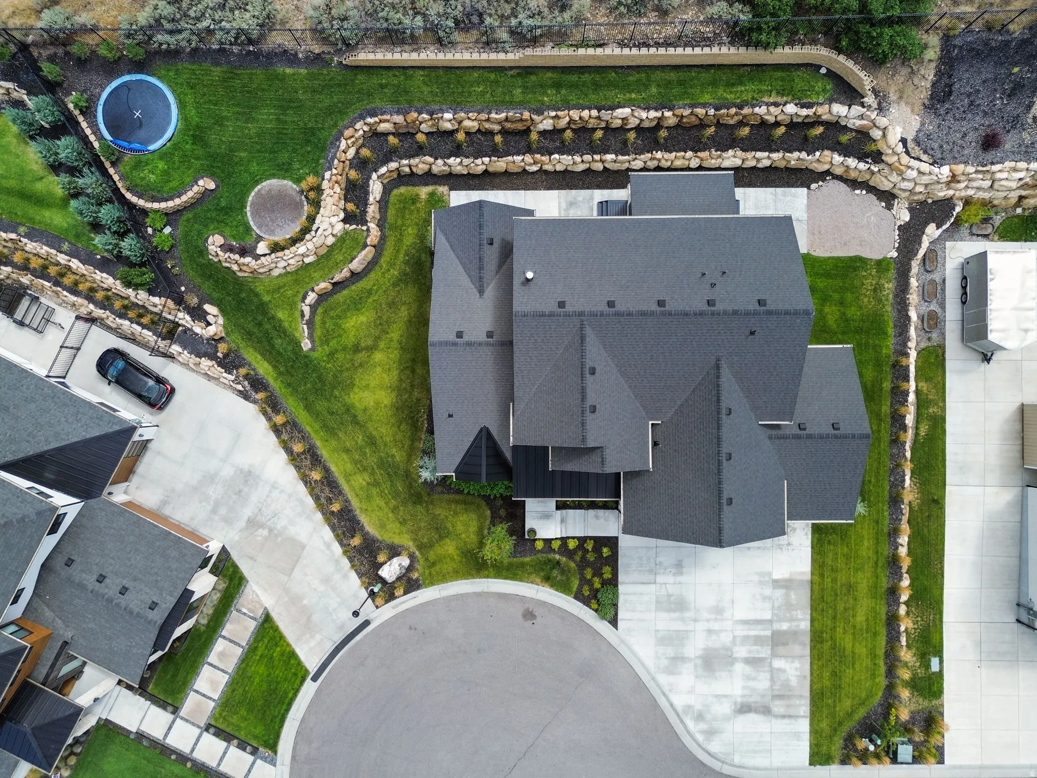 Expansive exterior featuring a dark-toned roof, concrete driveway, stone retaining walls, manicured lawns, and varied landscaping