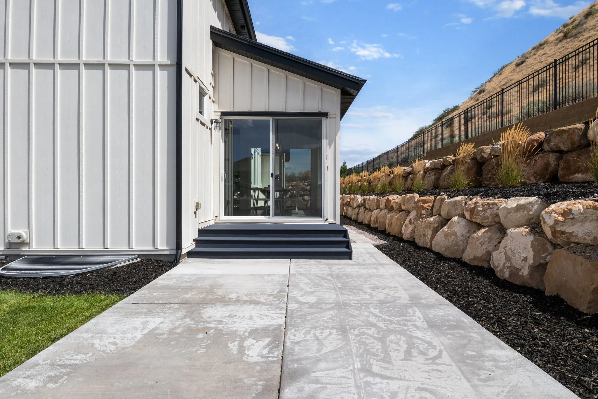 Sliding glass door, raised landing, exterior steps, concrete paver pathway, and rock retaining wall