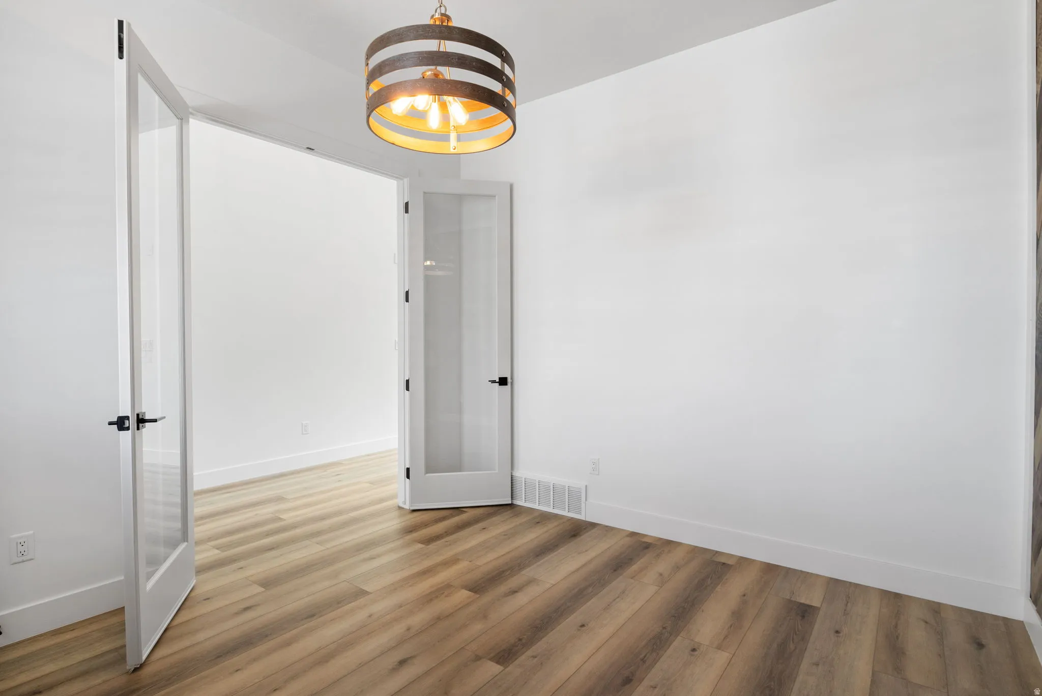 Wood-finish plank flooring, modern drum pendant light fixture, white walls, and French doors with matte black hardware