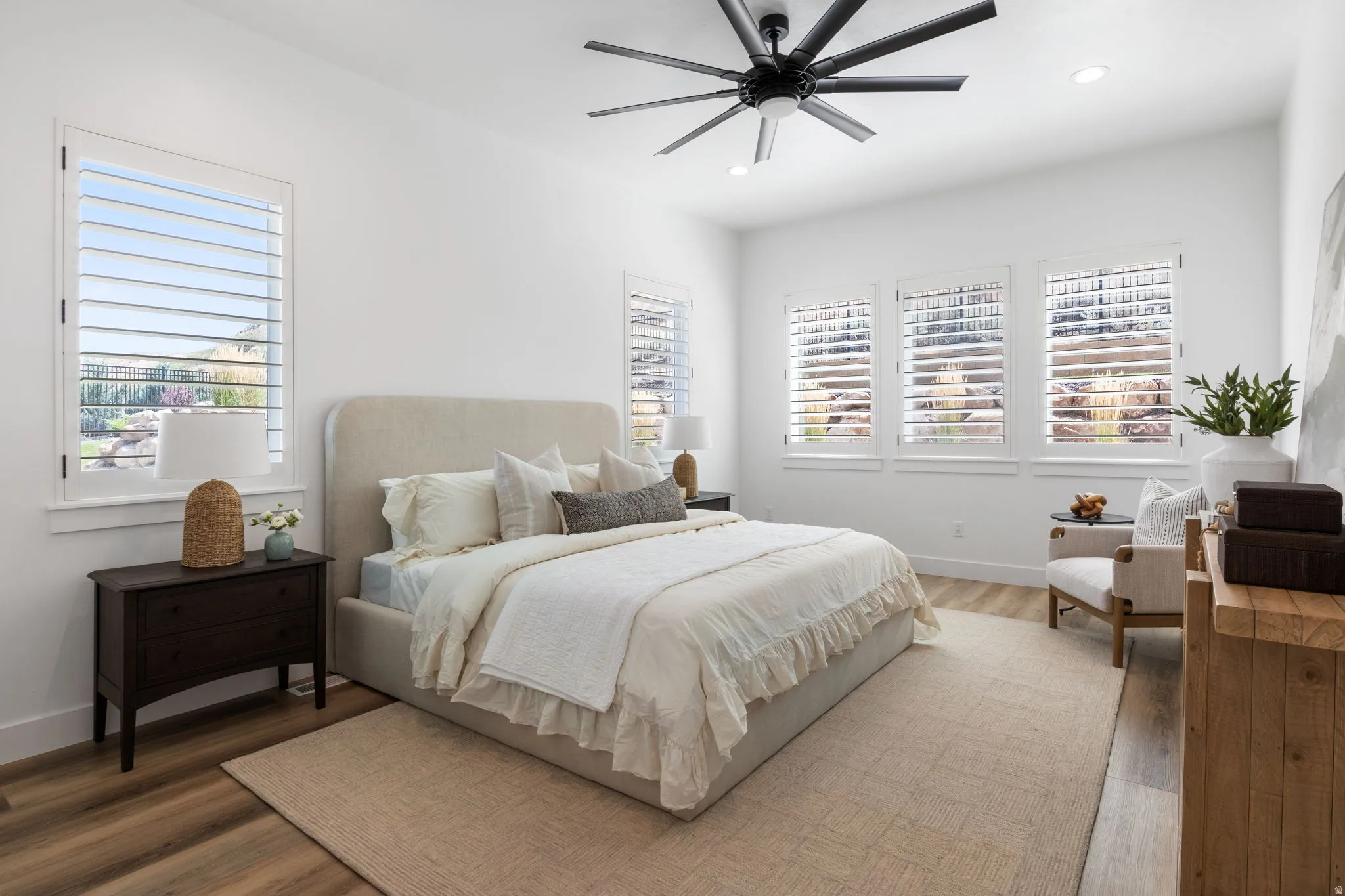 Spacious room featuring wood-finish flooring, multiple windows with plantation shutters, a ceiling fan, and recessed lighting