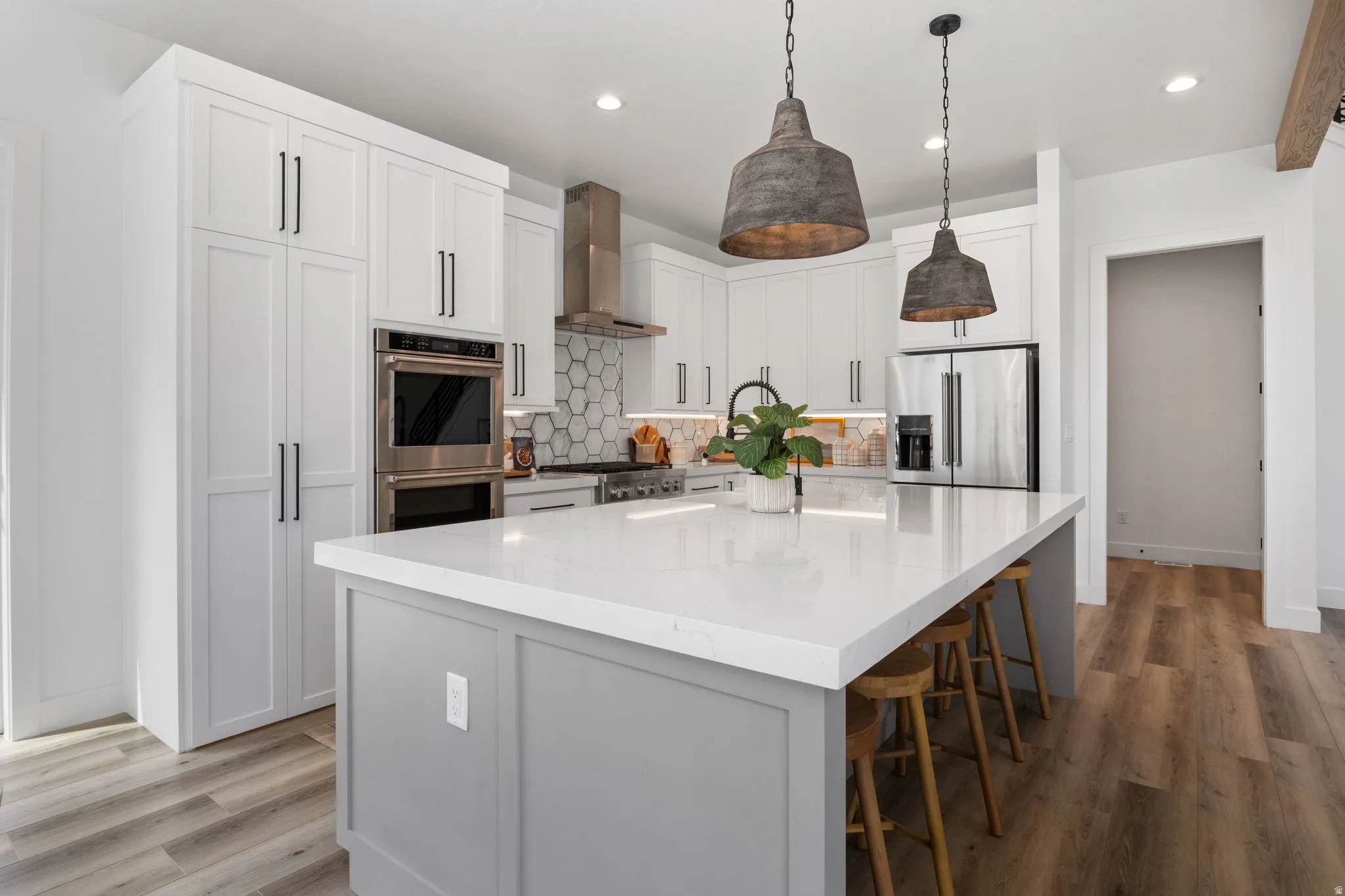 Kitchen featuring a central island with countertop seating, white shaker cabinetry, stainless steel appliances, a honeycomb tile backsplash, and wood-finish flooring