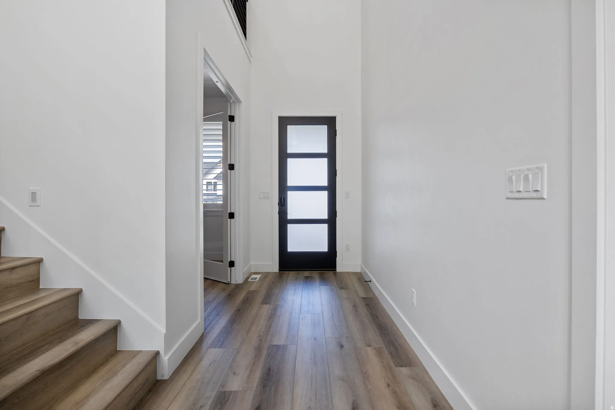 Entryway featuring a contemporary front door with frosted glass panels, wood-finish flooring, a light-toned wood staircase, and high ceilings