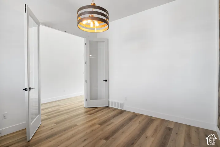 Wood-finish plank flooring, modern drum pendant light fixture, white walls, and French doors with matte black hardware