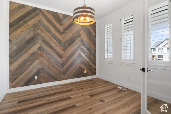 Herringbone wood-finish accent wall with wood-finish flooring, white walls, and three windows with white plantation shutters