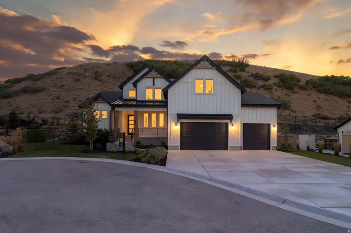 Modern farmhouse exterior with white board-and-batten siding, black gabled roof, two-car garage, concrete driveway, and mature landscaping