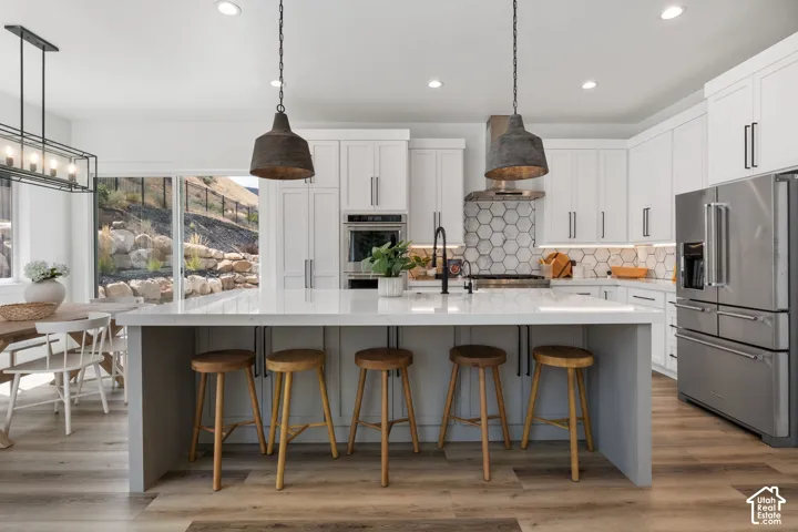Modern kitchen featuring an expansive island with a light-toned countertop, stainless steel appliances, white cabinetry, and wood-finish flooring