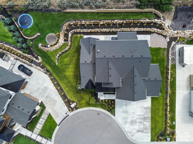 Expansive exterior featuring a dark-toned roof, concrete driveway, stone retaining walls, manicured lawns, and varied landscaping