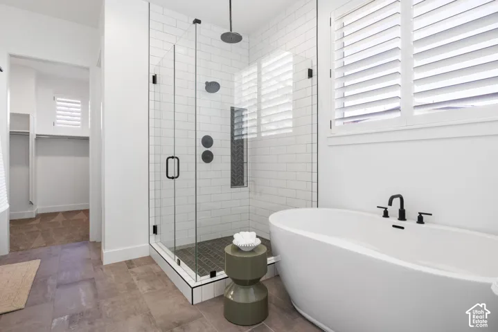 Freestanding soaking tub with matte black fixtures, glass-enclosed shower with subway tile surround, wood-finish flooring, and plantation shutters