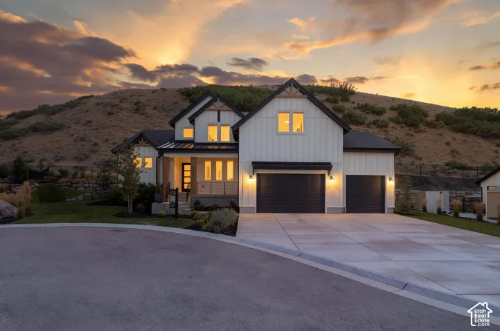 Modern farmhouse exterior with white board-and-batten siding, black gabled roof, two-car garage, concrete driveway, and mature landscaping