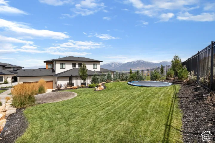 Expansive manicured lawn with a dark metal fence, mature landscaping, and mountain scenery